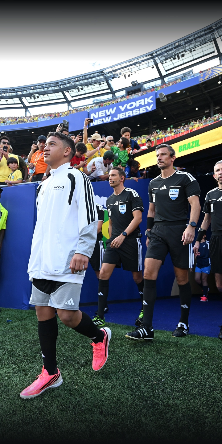 A child in a white kit leading the match officials out onto the pitch through the players' tunnel