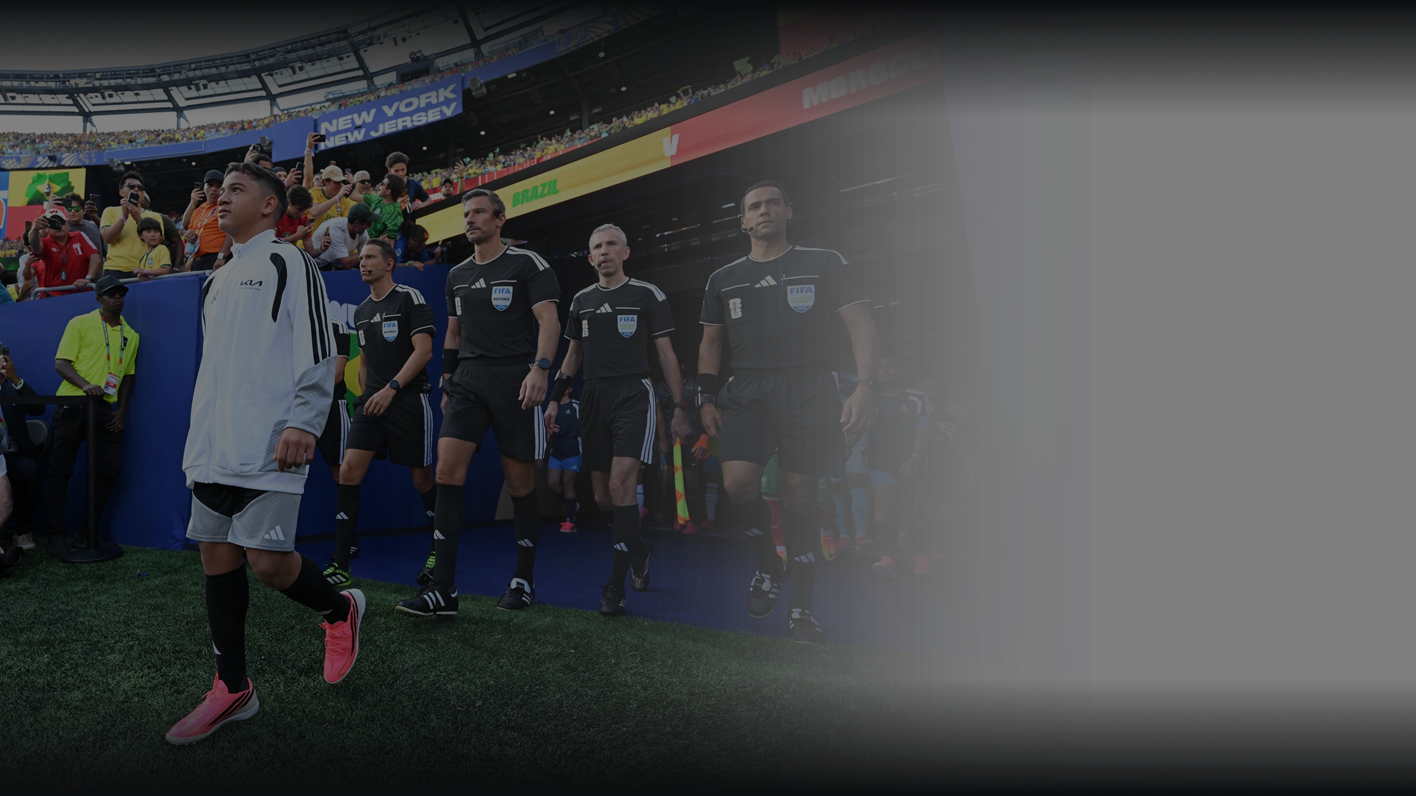 A child in a white kit leading the match officials out onto the pitch through the players' tunnel