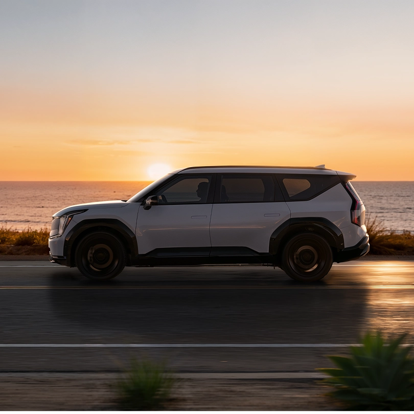 Kia SUV driving along a coastal road at sunset
