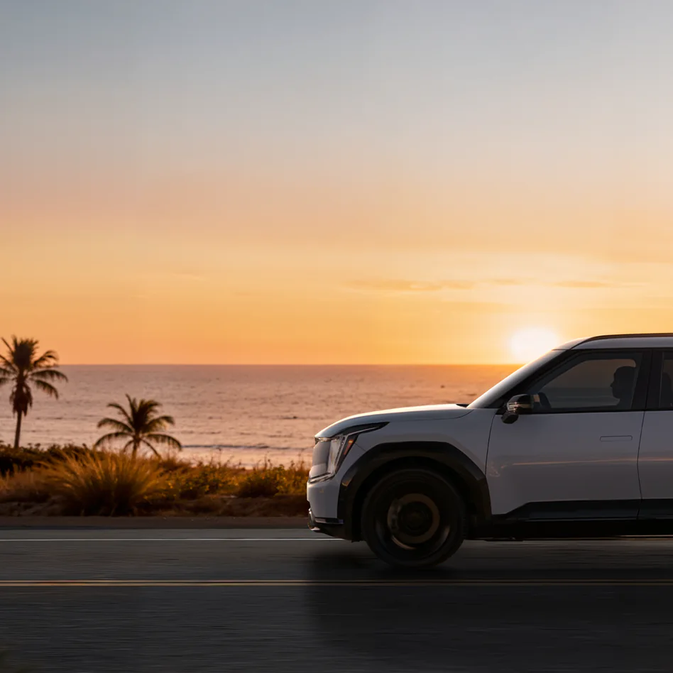 Kia SUV driving along a coastal road at sunset