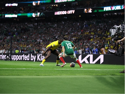 Two players challenging for the ball during a match, with Kia branding on the perimeter board behind them