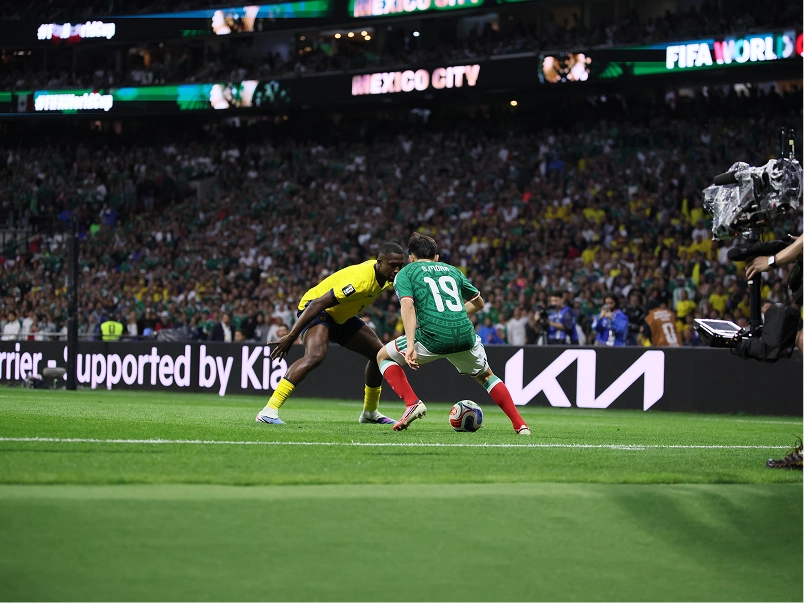 Two players challenging for the ball during a match, with Kia branding on the perimeter board behind them