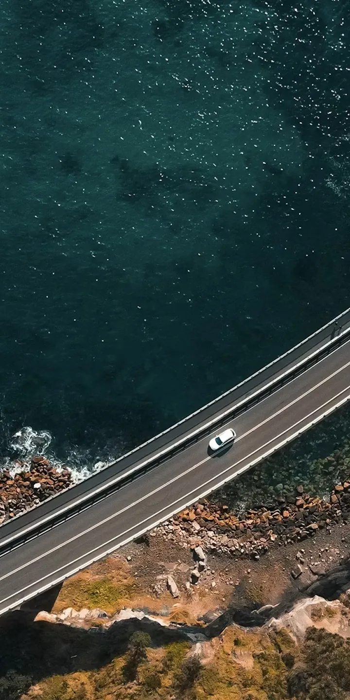 Aerial view of a vehicle driving along a coastal road between cliffs and the sea