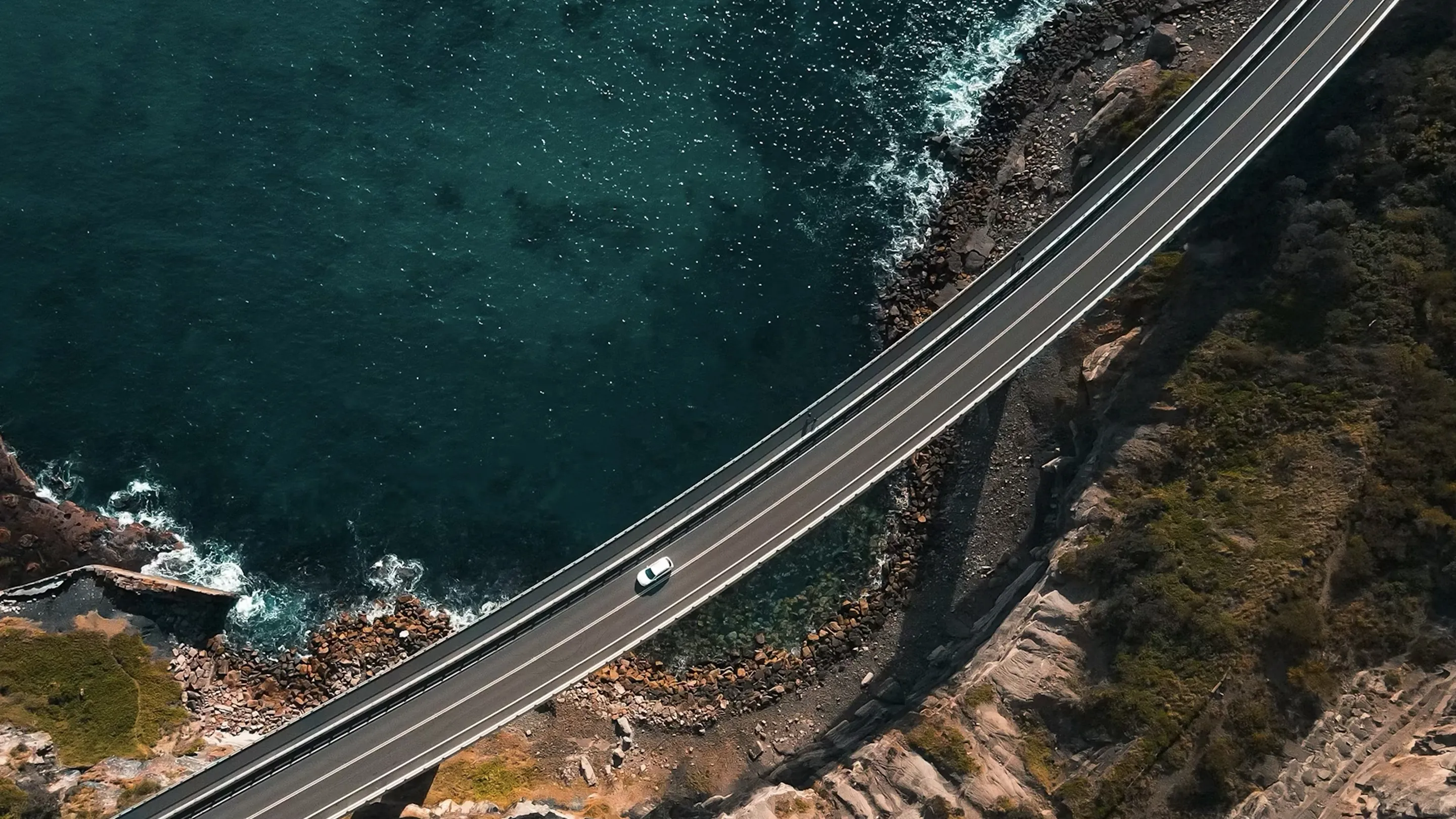 Aerial view of a vehicle driving along a coastal road between cliffs and the sea
