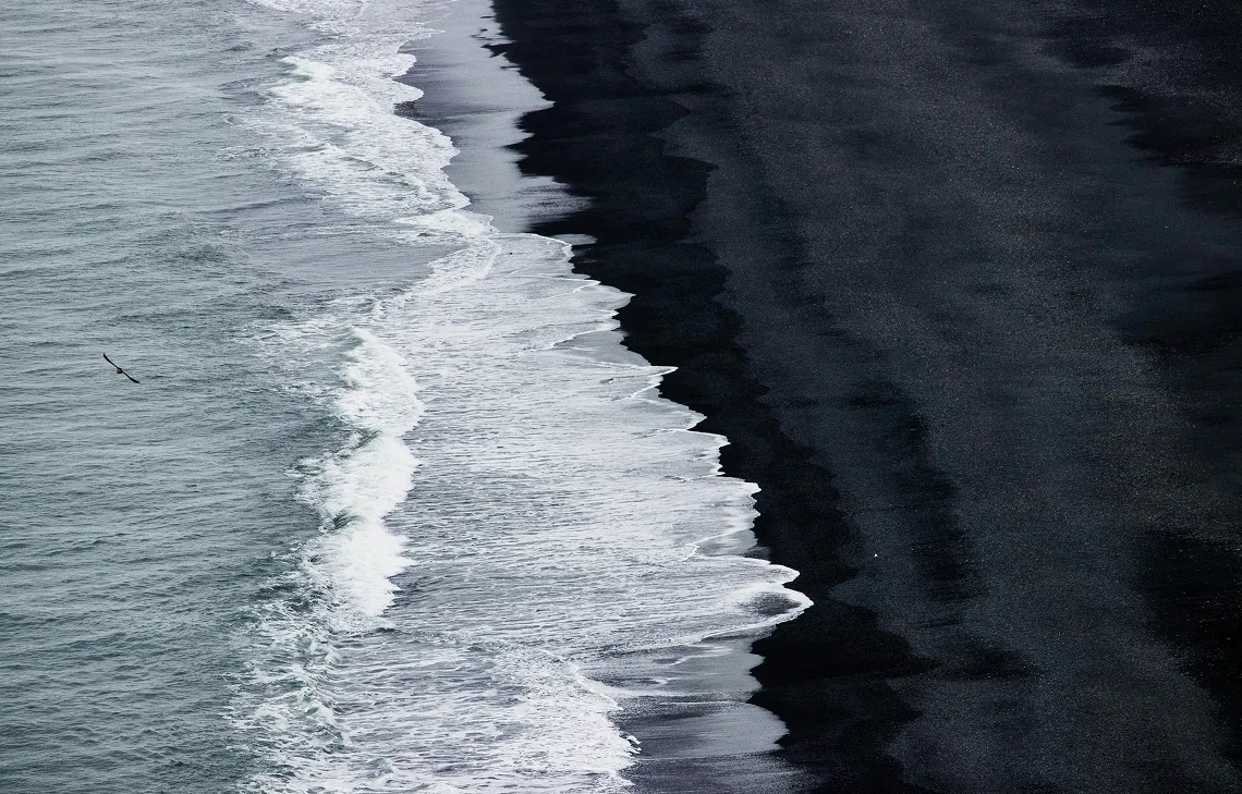 Aerial view of waves rolling onto a black sand beach