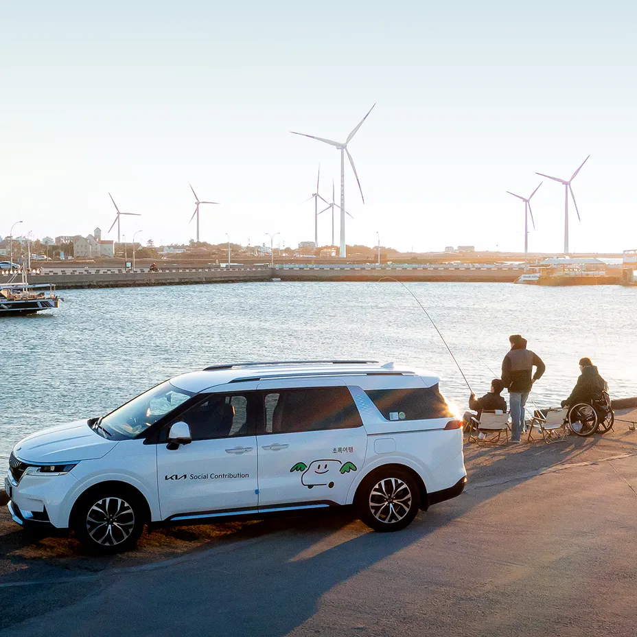 Coastal view with a Kia EV9 parked by the pier and wind turbines in the background