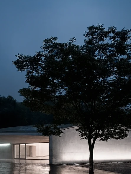 Image of an architectural space with trees and a building under night lighting