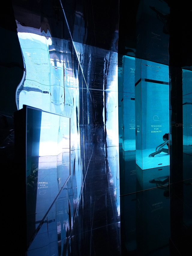 Exhibition space with blue-toned transparent panels and layered mirror reflections at the Gwangju Design Biennale.
