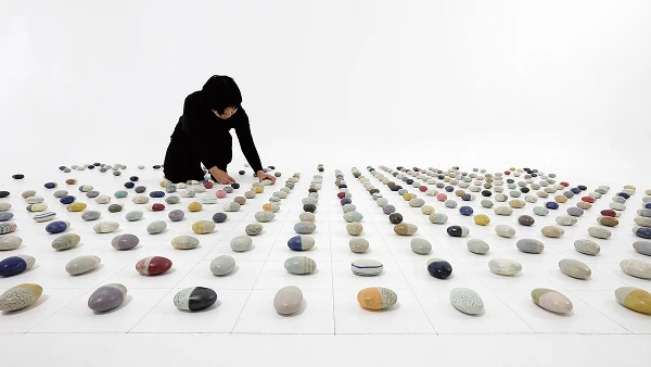 Image of a person arranging various ceramic objects placed on the floor