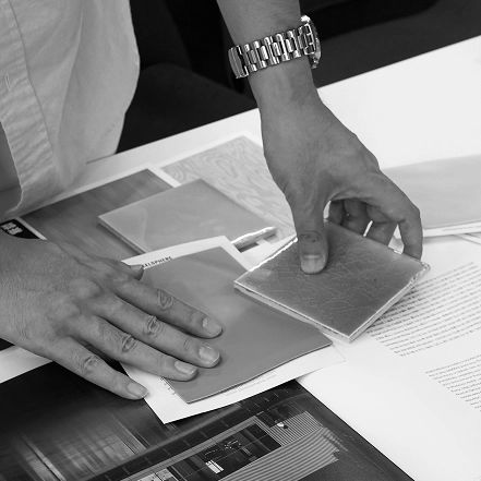Black-and-white image of hands examining material samples on a design table