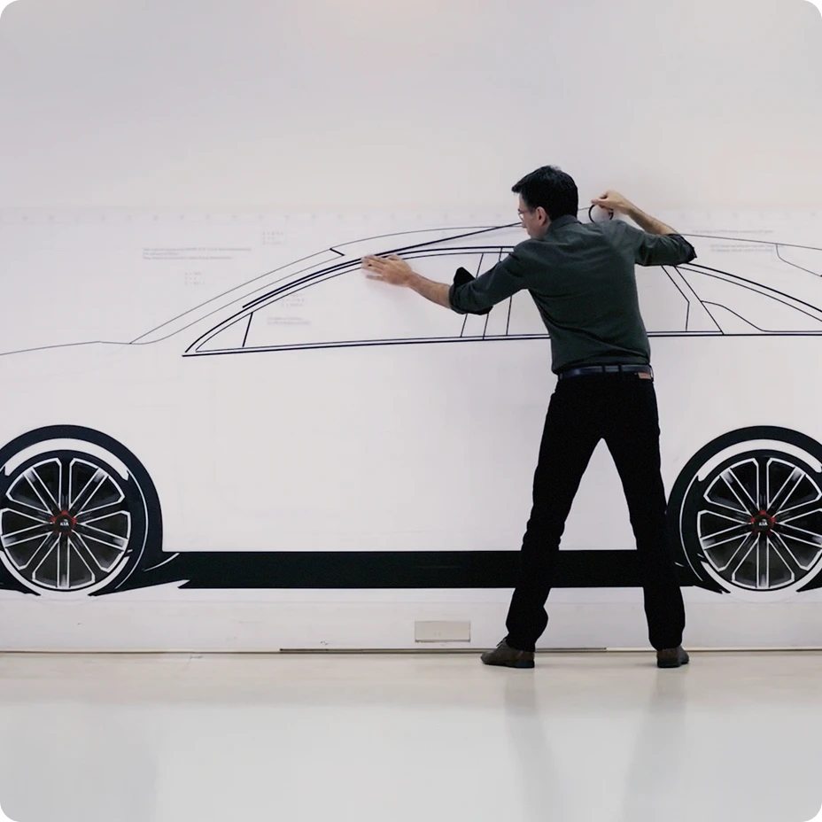Person refining a side-view sketch of a Kia vehicle drawn on a wall