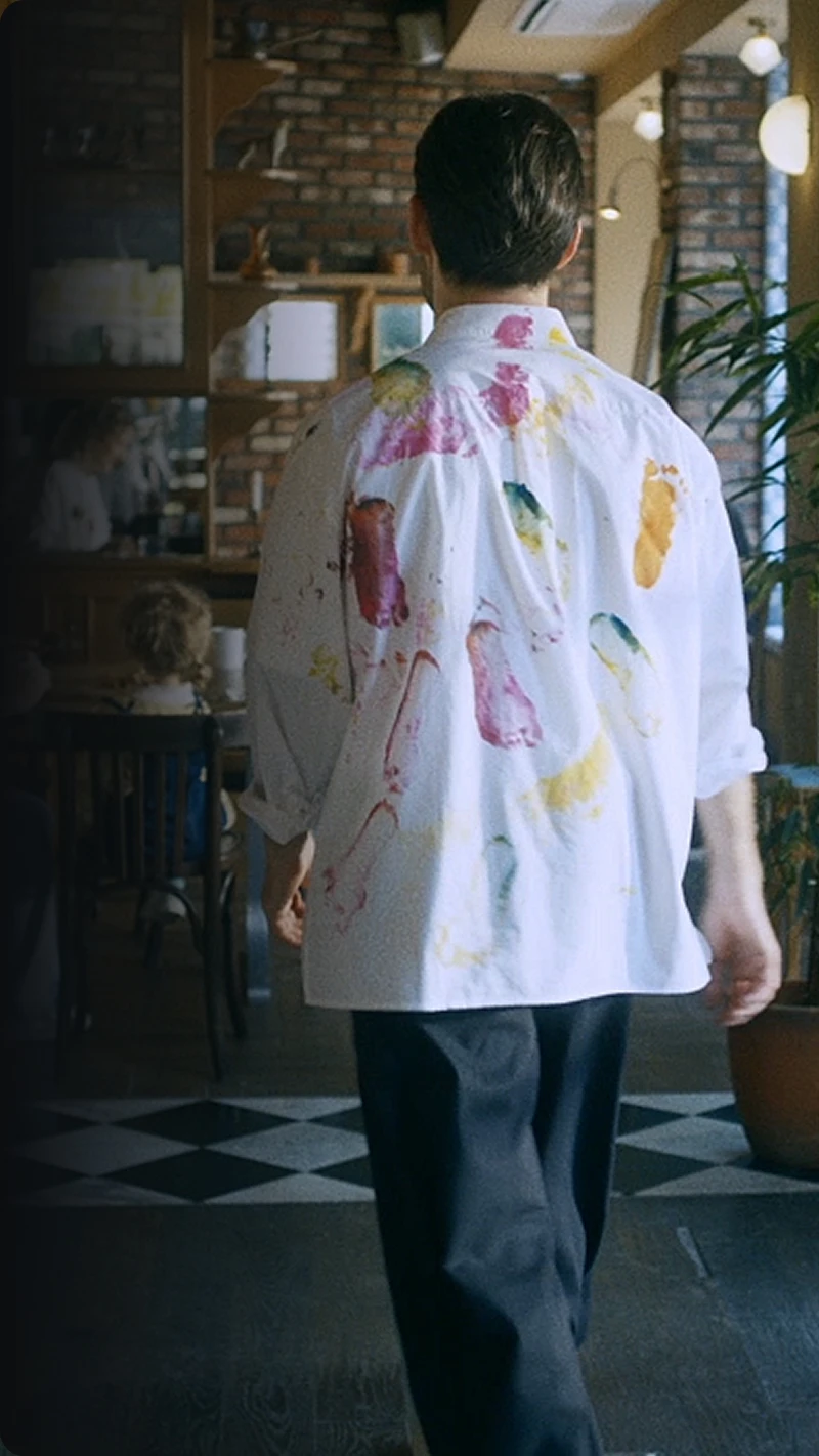 Back view of a person in a paint-stained shirt walking inside a café