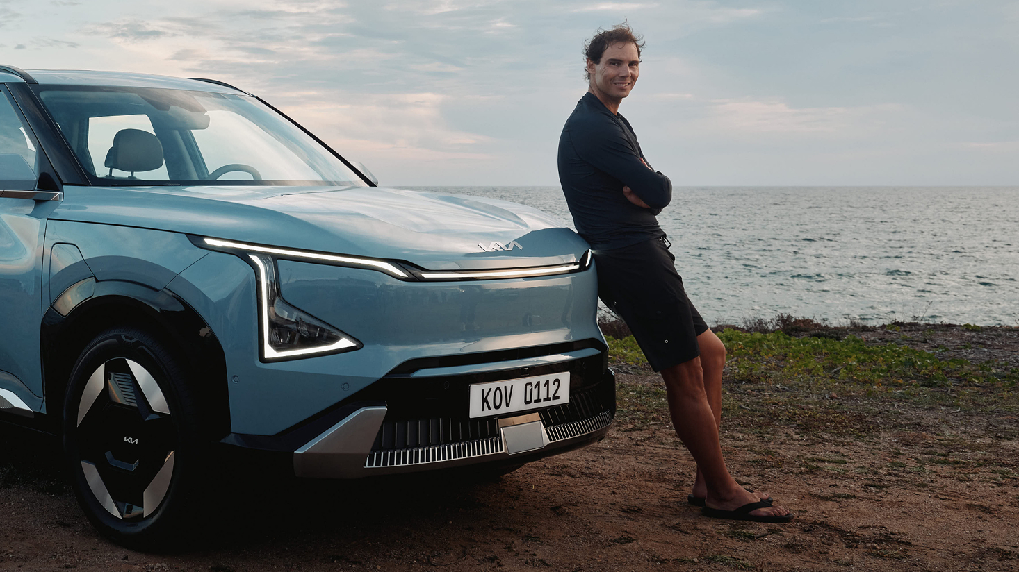 Rafael Nadal standing beside a Kia electric vehicle by the coast