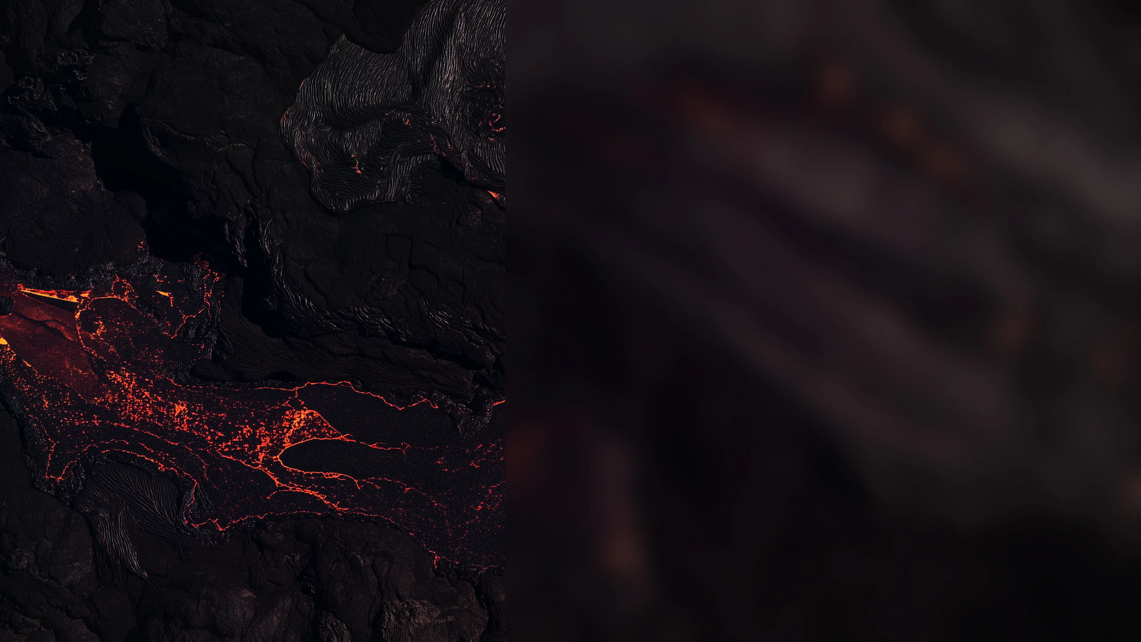 Close-up of red lava flowing over dark volcanic terrain.
