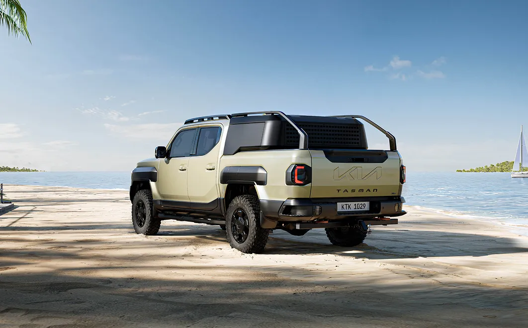 Rear three-quarter view of the Kia Tasman pickup truck with a coastal landscape behind