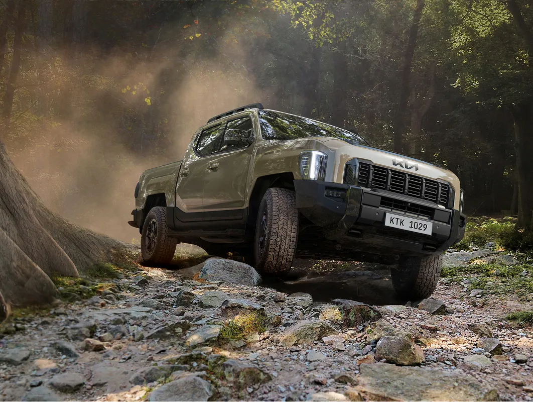 The Kia Tasman pickup truck driving through a forest off-road terrain