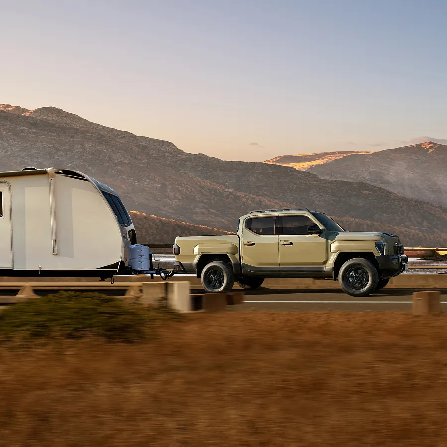 The Kia Tasman pickup truck towing a trailer while driving through a natural landscape