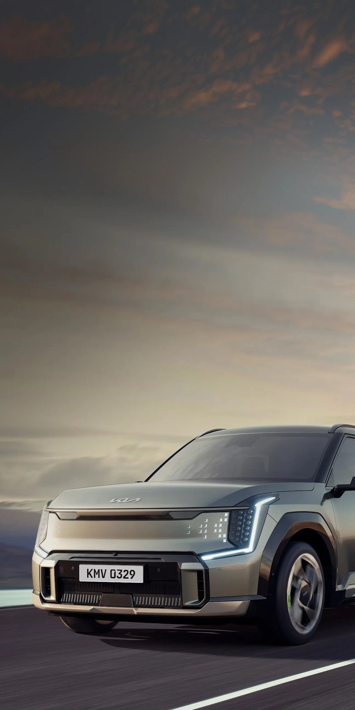 Front three-quarter view image of the Kia EV5 driving on a road with mountains in the background