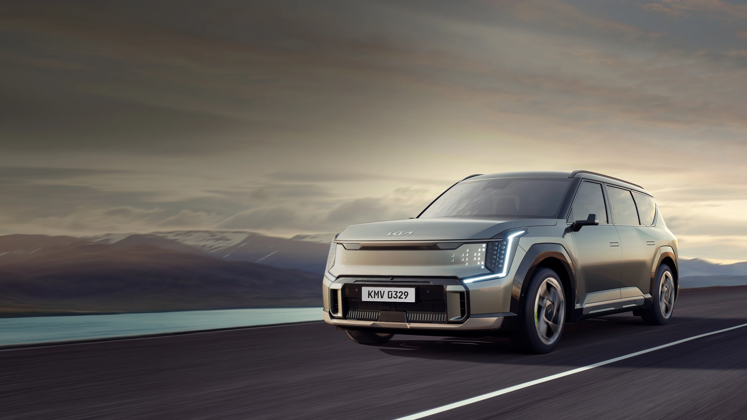 Front three-quarter view image of the Kia EV5 driving on a road with mountains in the background