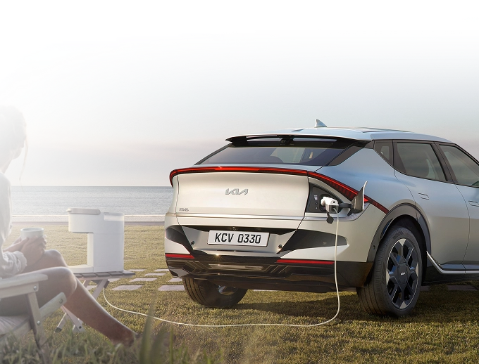 Rear three-quarter view image of the Kia EV6 charging via V2L outdoors